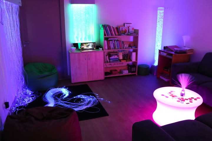 Cozy sensory room featuring colorful LED lighting, a bean bag chair, and a glowing table. The space includes a bookshelf, decorative elements, and flowing light strands, creating a relaxing atmosphere for sensory experiences. Cozy sensory room featuring colorful LED lighting, a bean bag chair, and a glowing table. The space includes a bookshelf, decorative elements, and flowing light strands, creating a relaxing atmosphere for sensory experiences.