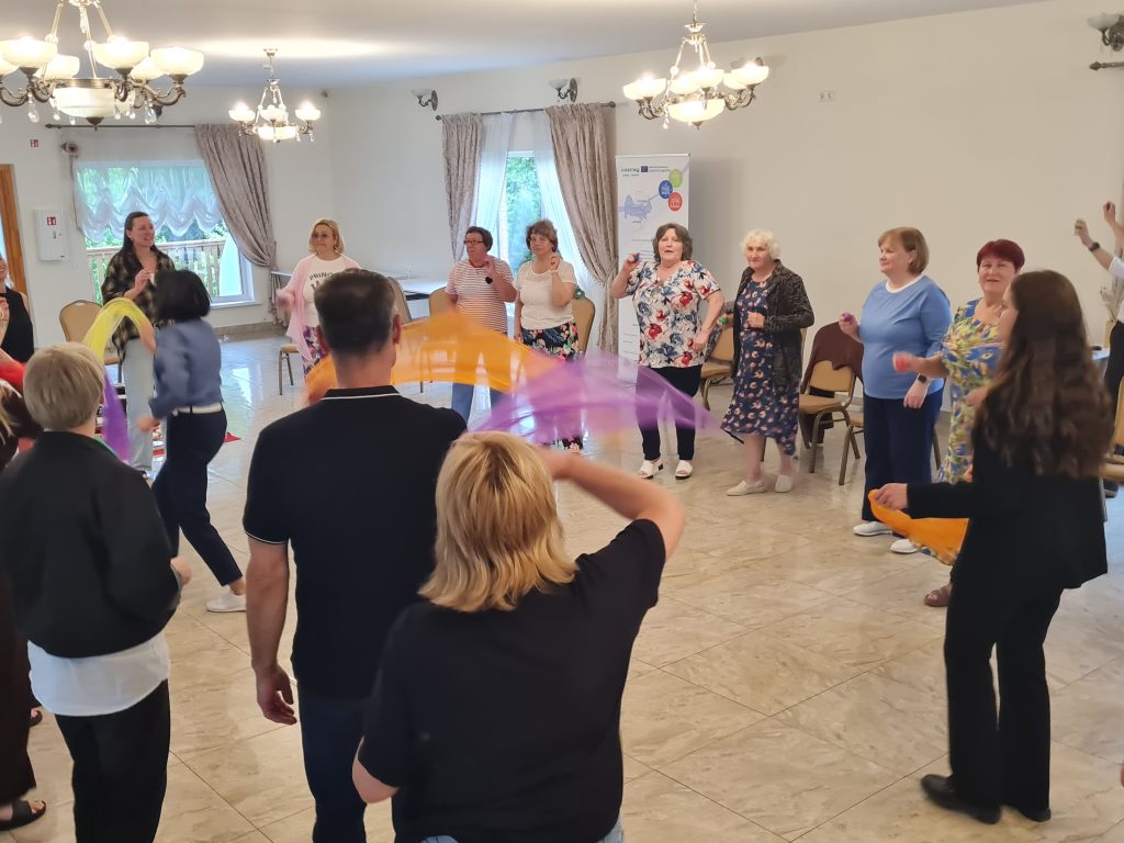 Group of adults engaging in a fun activity with colorful scarves in a spacious indoor setting, promoting social interaction and physical movement.