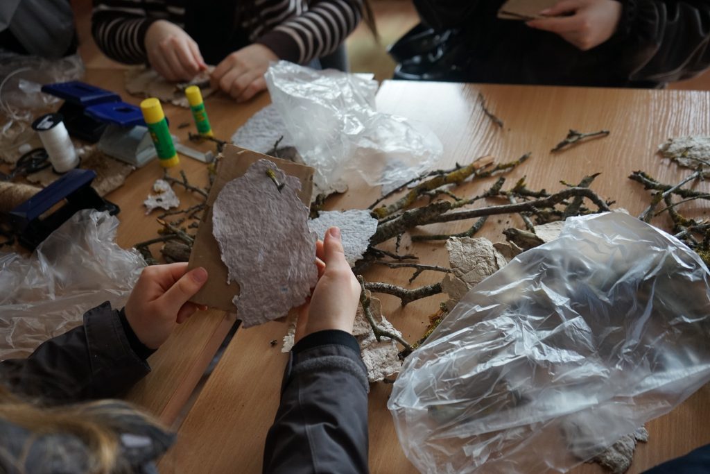 Participants engage in a hands-on crafting session, creating artworks with natural materials like bark and twigs, surrounded by tools and supplies on a wooden table.