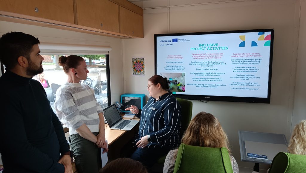 Group meeting discussing inclusive project activities related to the Sensory reading room initiative, with a presentation displayed on a screen. Participants are engaged, highlighting collaboration and community involvement in educational and social programs.