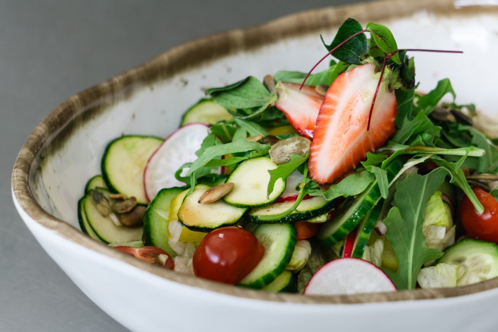 Fresh garden salad featuring sliced cucumbers, cherry tomatoes, radishes, arugula, and strawberries topped with pumpkin seeds, served in a rustic bowl. Perfect for healthy eating and vibrant meals.