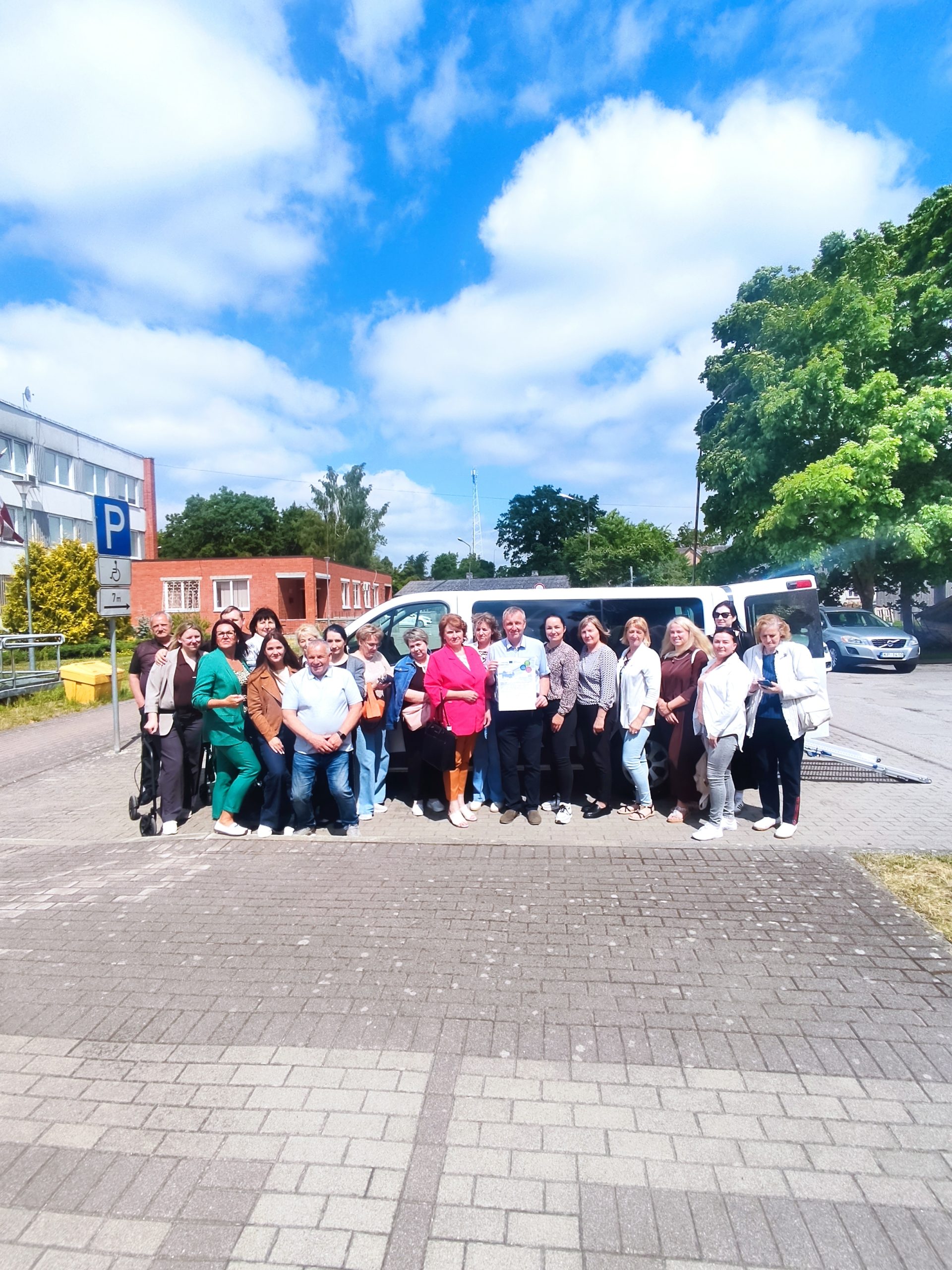 Group photo of a diverse gathering of individuals smiling outdoors in a parking area, with a blue sky and fluffy clouds in the background. The group is standing in front of a van and surrounded by greenery, showcasing camaraderie and community spirit. Group photo of a diverse gathering of individuals smiling outdoors in a parking area, with a blue sky and fluffy clouds in the background. The group is standing in front of a van and surrounded by greenery, showcasing camaraderie and community spirit.