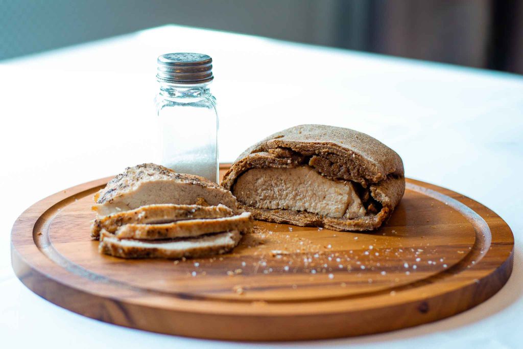 Sliced homemade bread on a wooden cutting board with a small salt shaker, showcasing a soft interior and rustic crust.