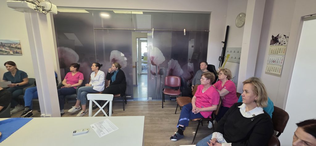 Group of healthcare personnel attending initial training for the “ElderGuardian” project, seated in a modern training room with floral decor and instructional materials visible.
