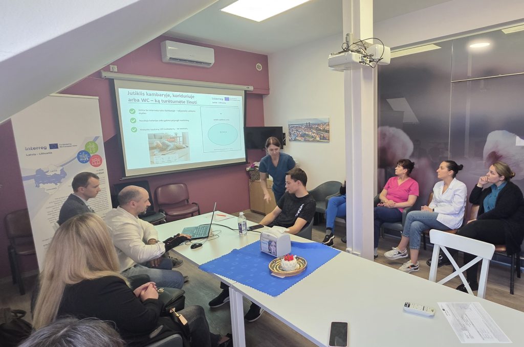 Group training session for the "ElderGuardian" project, featuring personnel engaged in discussions and presentations about the project's final implementation stage. A projector displays relevant information while participants interact and take notes in a collaborative environment.