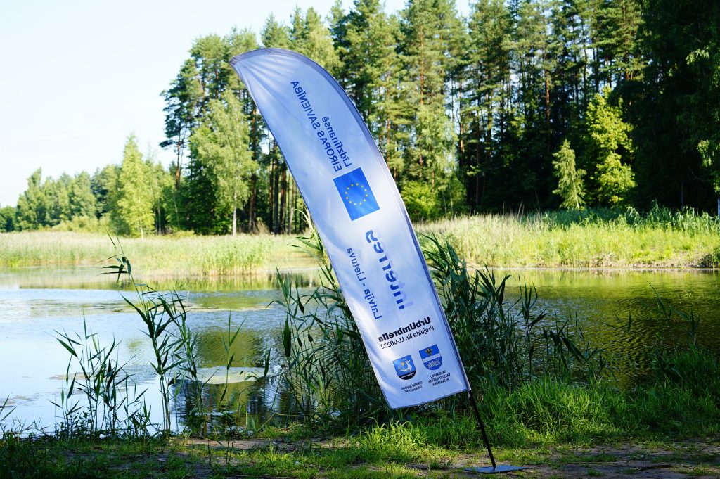 Flag displaying European Union logos near the water at Ruģeļi Wetland in Daugavpils, Latvia, highlighting environmental conservation efforts for turtle release.