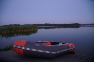 Inflatable boat resting on a dock at twilight, with calm water and lush greenery in the background, ideal for fishing or recreational activities.