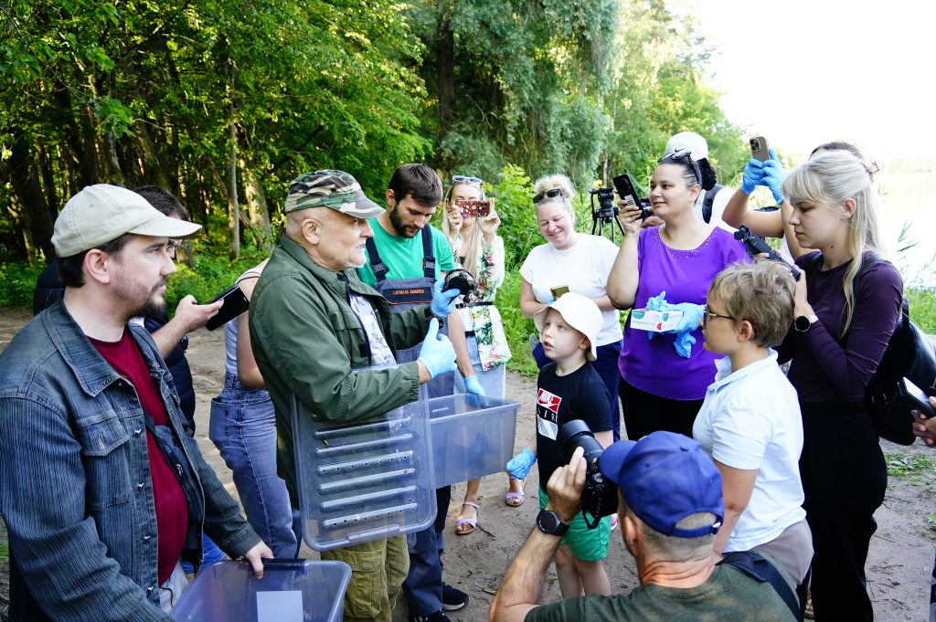 Participants gather at the Ruģeļi Wetland in Daugavpils, Latvia, to witness the release of turtles into the wild, with a focus on education and wildlife conservation.