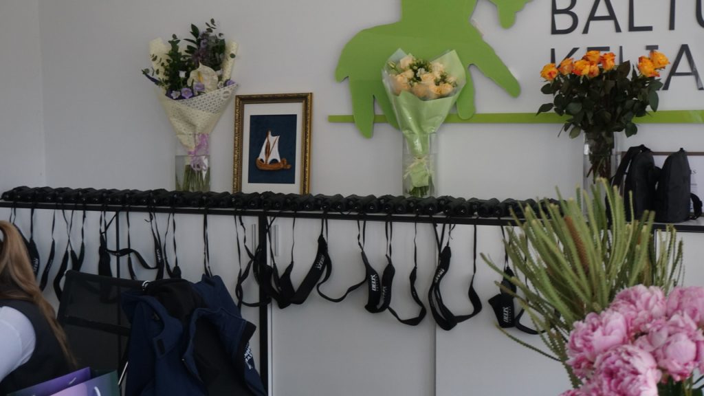 Interior view of a room showcasing flowers and a decorative wall art piece, with a rack displaying multiple headsets, highlighting the setting for the BIRDIE project partner meeting in the Klaipėda region.