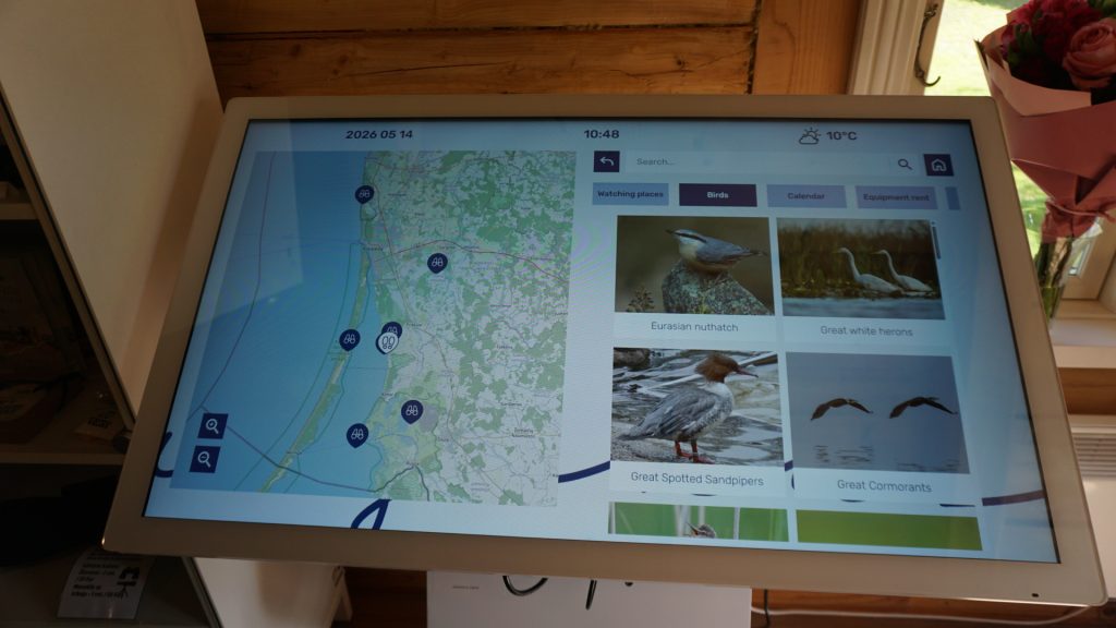Interactive touchscreen display showcasing a map of the Klaipėda region, featuring birdwatching locations and images of local bird species including the Eurasian nuthatch, Great white herons, Great Spotted Sandpipers, and Great Cormorants.