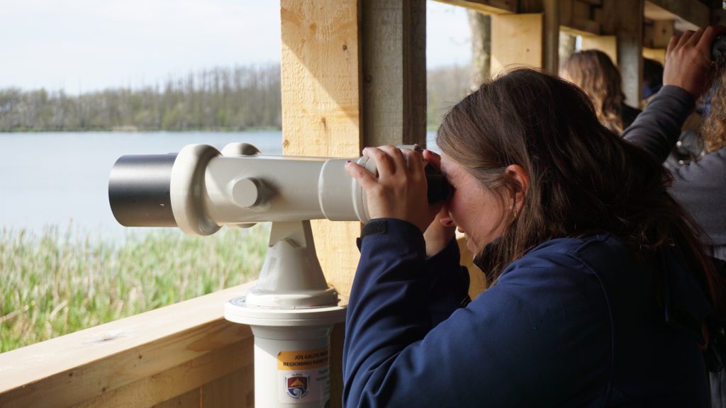 A woman using a telescope to observe wildlife at a viewing platform near a lake in the Klaipėda region, highlighting the BIRDIE project’s focus on environmental exploration and biodiversity.