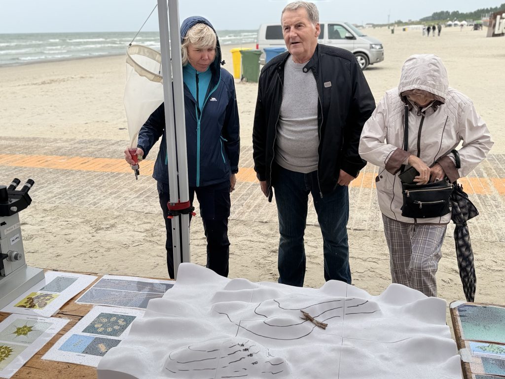 Visitors exploring a beach science exhibit, featuring a microscope and educational materials, on a cloudy day by the ocean. Visitors exploring a beach science exhibit, featuring a microscope and educational materials, on a cloudy day by the ocean.