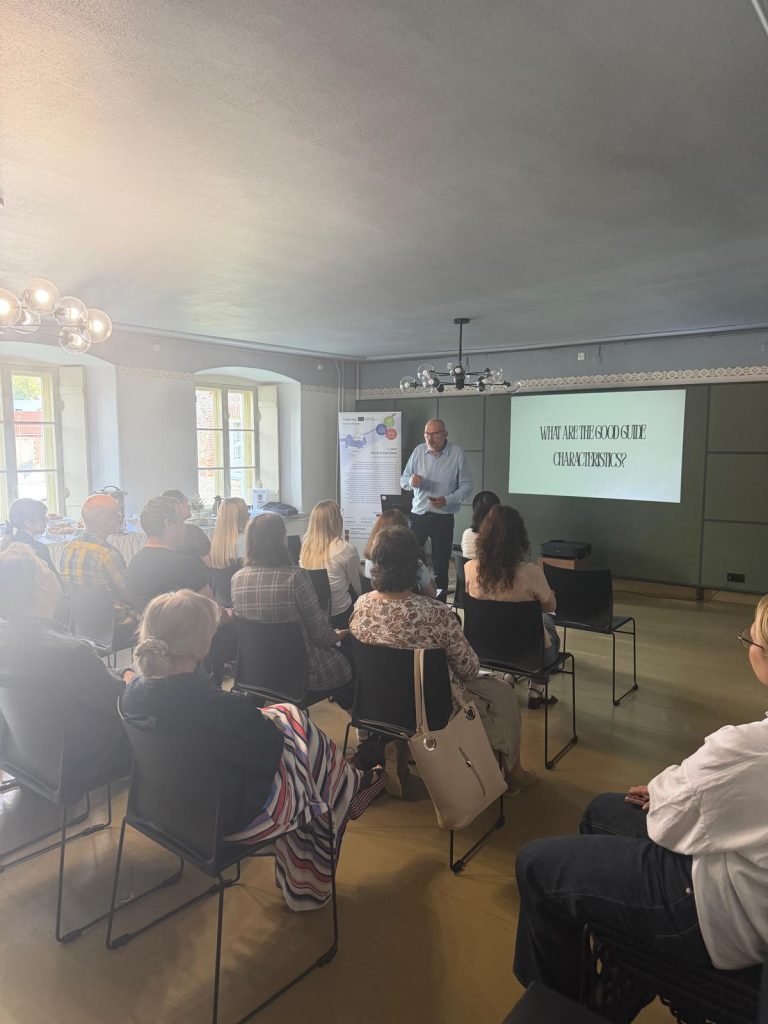 Lecture for tourism professionals and guides at Krustpils Castle, featuring a speaker discussing the characteristics of effective tour guides, with an engaged audience seated in a modern classroom setting.