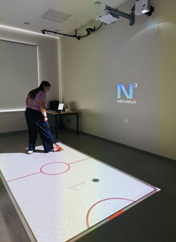 A woman interacts with a projected interactive game on a digital surface designed for rehabilitation, showcasing innovative technology in the SPEED UP Project.
