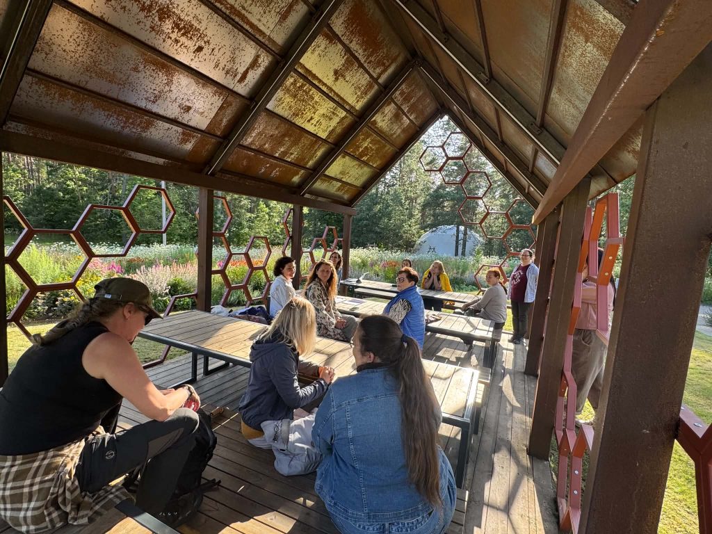 Group of people engaged in a discussion under a unique hexagonal pavilion surrounded by a vibrant garden, illustrating collaborative learning experiences from the Green Stories Project. Group of people engaged in a discussion under a unique hexagonal pavilion surrounded by a vibrant garden, illustrating collaborative learning experiences from the Green Stories Project.