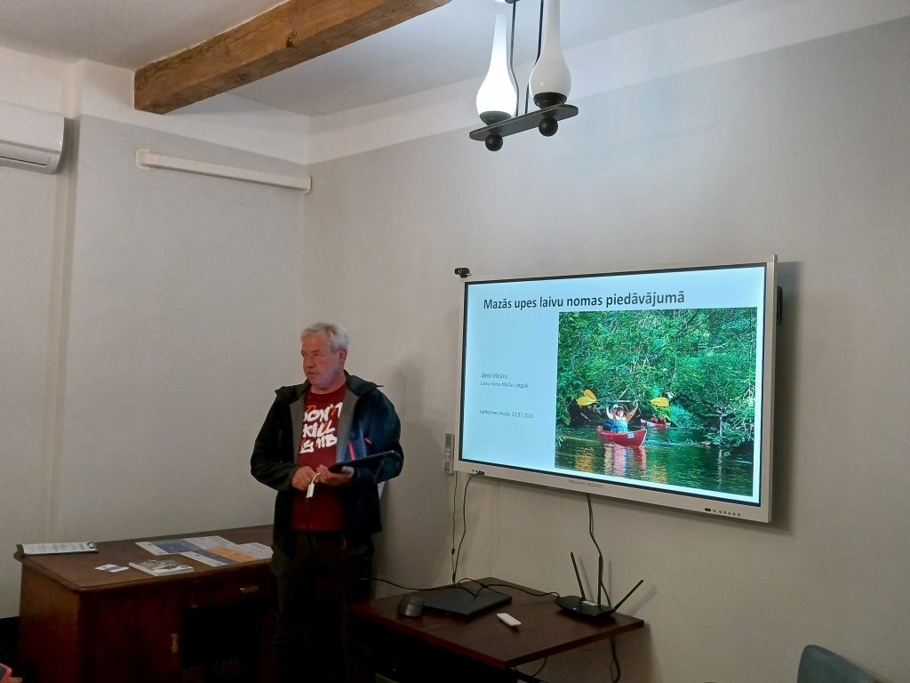 Speaker presenting at the "Water Tourism Trends in Latgale" seminar at Lielborne Manor, with a slide showcasing kayaking on a small river, highlighting local boat rental services.