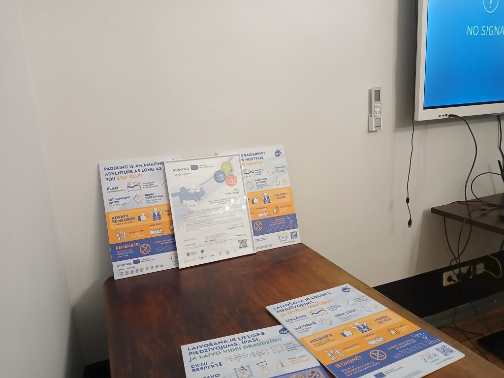Informative display materials on water tourism safety and guidelines at the industry seminar in Lielborne Manor, Latgale, featuring colorful posters and a digital screen.