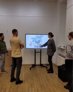 Group of professionals discussing the MATOMI project, with a focus on modern museum experiences, while referencing a digital presentation displayed on a screen.