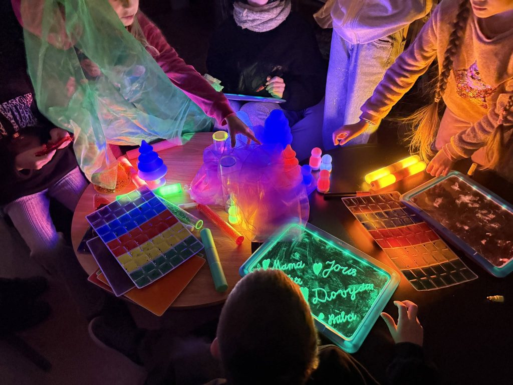 Children engaging in creative activities with glowing materials on a table, showcasing colorful tools and items related to the INCLUSIVE project, emphasizing collaboration and exploration. Children engaging in creative activities with glowing materials on a table, showcasing colorful tools and items related to the INCLUSIVE project, emphasizing collaboration and exploration.