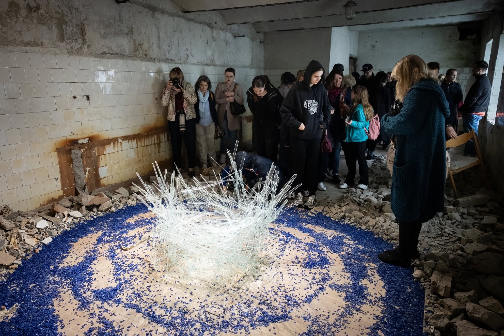 Visitors observe an art installation made of glass and blue materials at the JEWEL Art Residency in Žagarė, showcasing creativity in a rustic, partially ruined space. Visitors observe an art installation made of glass and blue materials at the JEWEL Art Residency in Žagarė, showcasing creativity in a rustic, partially ruined space.
