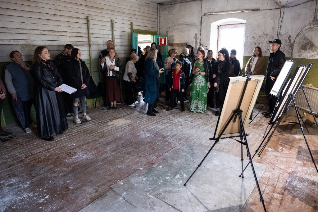 A group of attendees gathered in a rustic room during the JEWEL Art Residency event in Žagarė, featuring an array of easels displaying artwork. The participants, dressed in various styles, engage in conversation and observe the art, highlighting the community's involvement in the residency program. A group of attendees gathered in a rustic room during the JEWEL Art Residency event in Žagarė, featuring an array of easels displaying artwork. The participants, dressed in various styles, engage in conversation and observe the art, highlighting the community's involvement in the residency program.