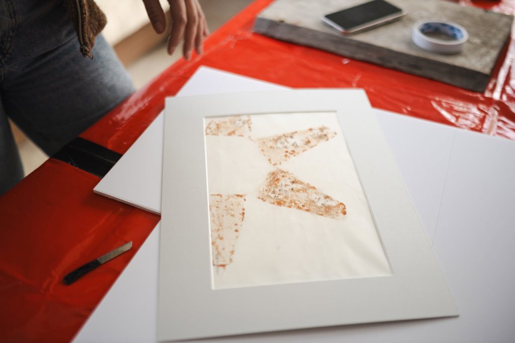 Artistic piece created during the JEWEL Art Residency in Žagarė, displayed on a red table with framing materials and tools visible. Artistic piece created during the JEWEL Art Residency in Žagarė, displayed on a red table with framing materials and tools visible.