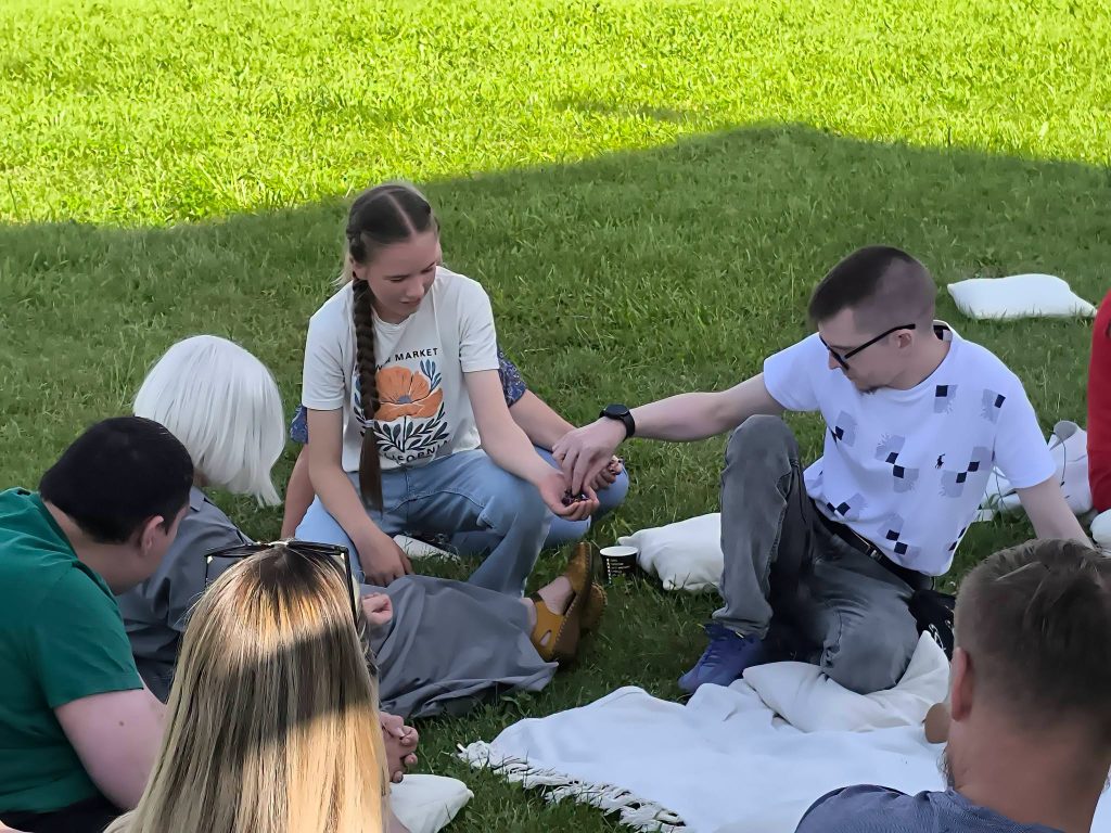 Participants engaged in an interactive educational workshop titled "Bee Guide," sitting on the grass, practicing teamwork and communication skills through hands-on activities. Participants engaged in an interactive educational workshop titled "Bee Guide," sitting on the grass, practicing teamwork and communication skills through hands-on activities.