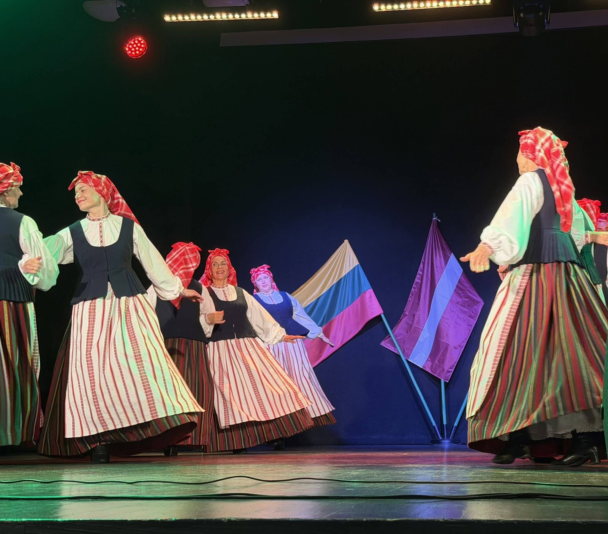Traditional dancers in vibrant costumes perform on stage, celebrating Lithuanian and Latvian cultural heritage, with the flags of both countries displayed in the background.