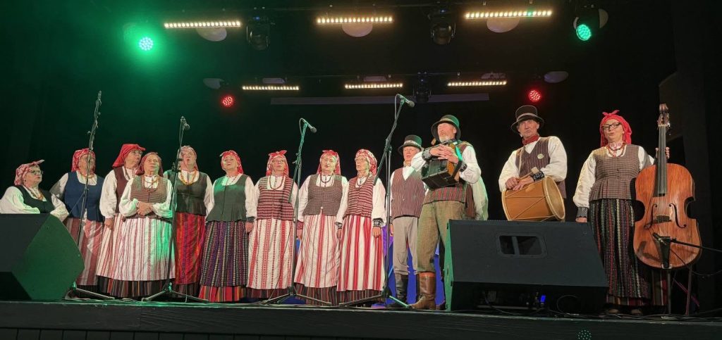 Traditional folk singers in colorful costumes perform on stage during a musical event celebrating Lithuanian and Latvian traditions in Baisogala, featuring various traditional instruments.