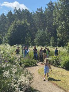 Group of adults and children engaging in nature exploration in a lush garden setting, surrounded by wildflowers and trees, highlighting educational experiences from the Green Stories Project. A young girl walks along a winding path, embodying the spirit of outdoor learning and environmental connection. Group of adults and children engaging in nature exploration in a lush garden setting, surrounded by wildflowers and trees, highlighting educational experiences from the Green Stories Project. A young girl walks along a winding path, embodying the spirit of outdoor learning and environmental connection.