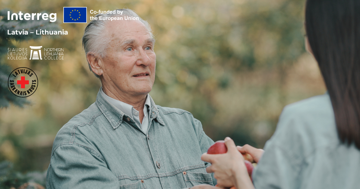 Elderly man receiving apples from a volunteer in a natural setting, symbolizing peer support and community engagement for active aging. The image is part of the ACE Volunteer Training program, co-funded by the European Union, promoting health and well-being among seniors in Latvia and Lithuania.