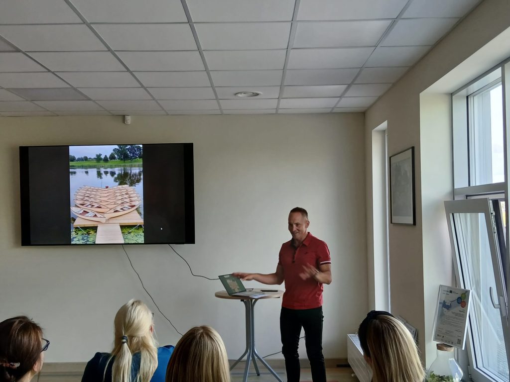 Speaker presenting at the seminar "Water Tourism Trends in Zemgale" in Jelgava, with a slideshow featuring a wooden boat dock on a tranquil lake. Attendees are engaged in the discussion, highlighting the importance of water tourism in the region. Speaker presenting at the seminar "Water Tourism Trends in Zemgale" in Jelgava, with a slideshow featuring a wooden boat dock on a tranquil lake. Attendees are engaged in the discussion, highlighting the importance of water tourism in the region.