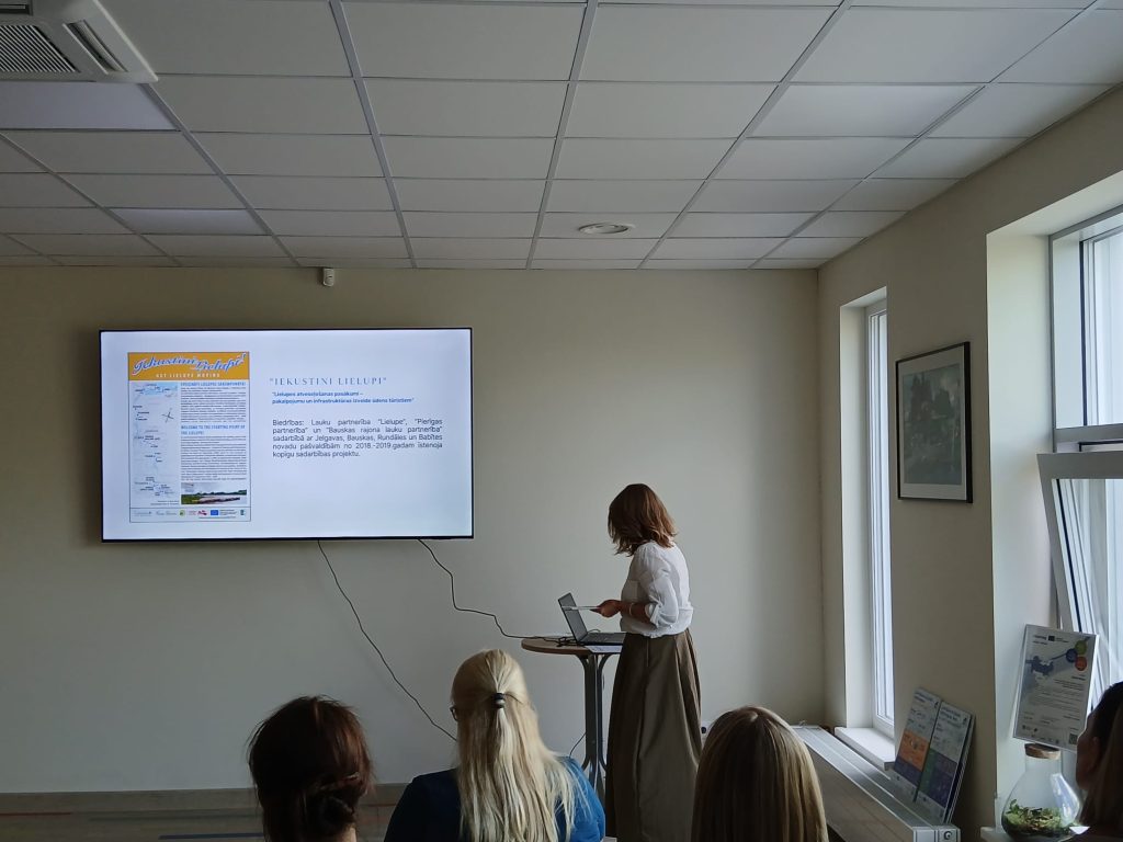 A speaker presents at the seminar "Water Tourism Trends in Zemgale" in Jelgava, with a digital screen displaying information about the "Iekustini Lielupi" project, while attendees engage in the discussion. A speaker presents at the seminar "Water Tourism Trends in Zemgale" in Jelgava, with a digital screen displaying information about the "Iekustini Lielupi" project, while attendees engage in the discussion.
