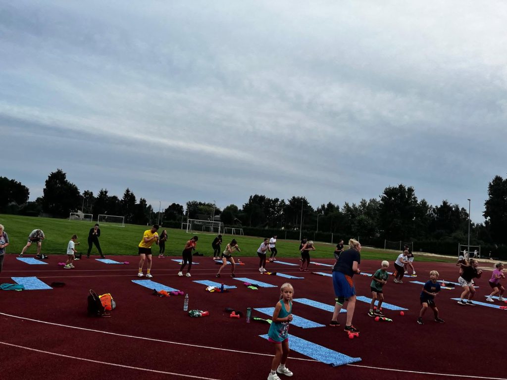 Participants engaging in fitness activities on a track, using mats and weights, as part of the Healthy Lifestyle “A Billion Steps Challenge” (BISTEPS) project. The scene includes children and adults exercising together outdoors in a community health initiative.