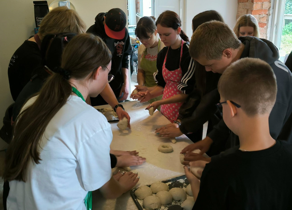 Young people engaged in a hands-on baking activity, shaping dough on a floured table as part of the Action! Jewel-26 program, which focuses on exploring Jewish heritage through filmmaking and cultural experiences.