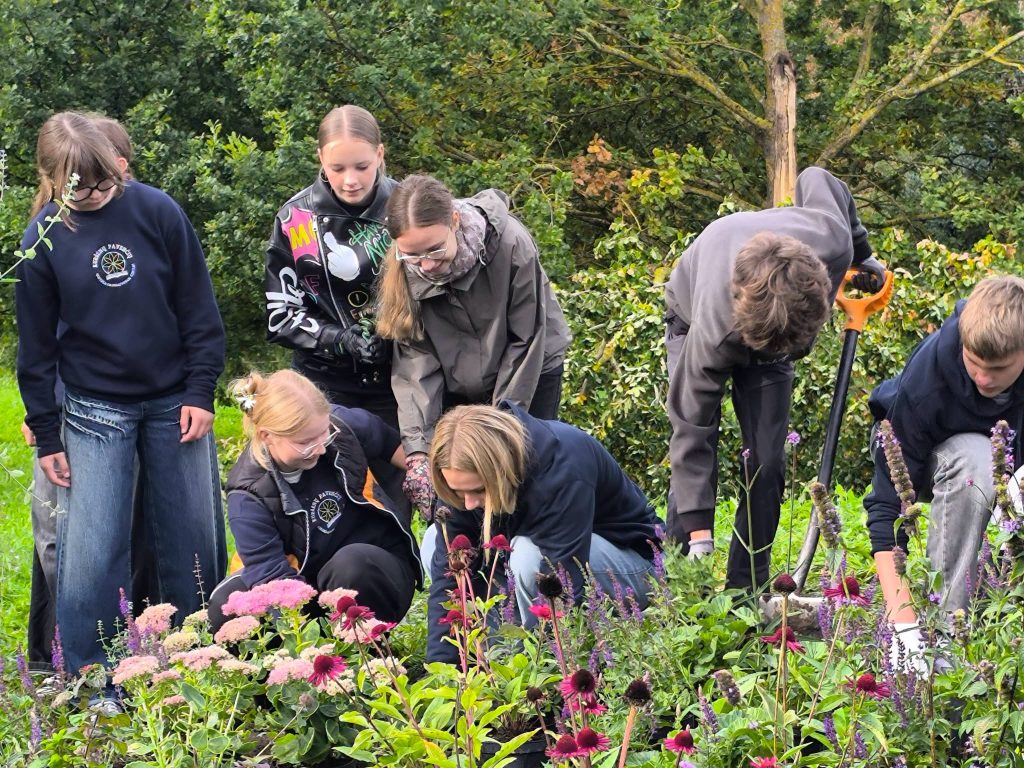 A group of children actively gardening in a vibrant bee garden, planting flowers and tending to plants, surrounded by lush greenery in the Youth Garden.