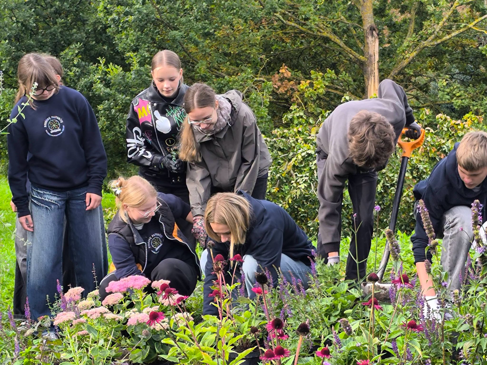 A group of children actively gardening in a vibrant bee garden, planting flowers and tending to plants, surrounded by lush greenery in the Youth Garden.