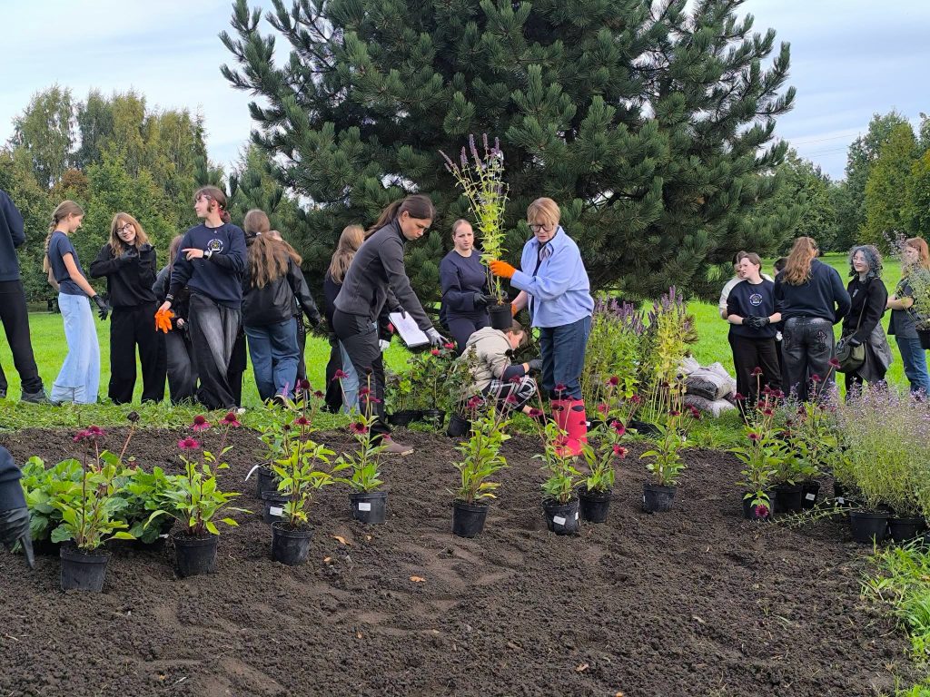 A group of young volunteers planting flowers in a bee garden at the Youth Garden, surrounded by greenery and potted plants, promoting environmental awareness and community involvement.