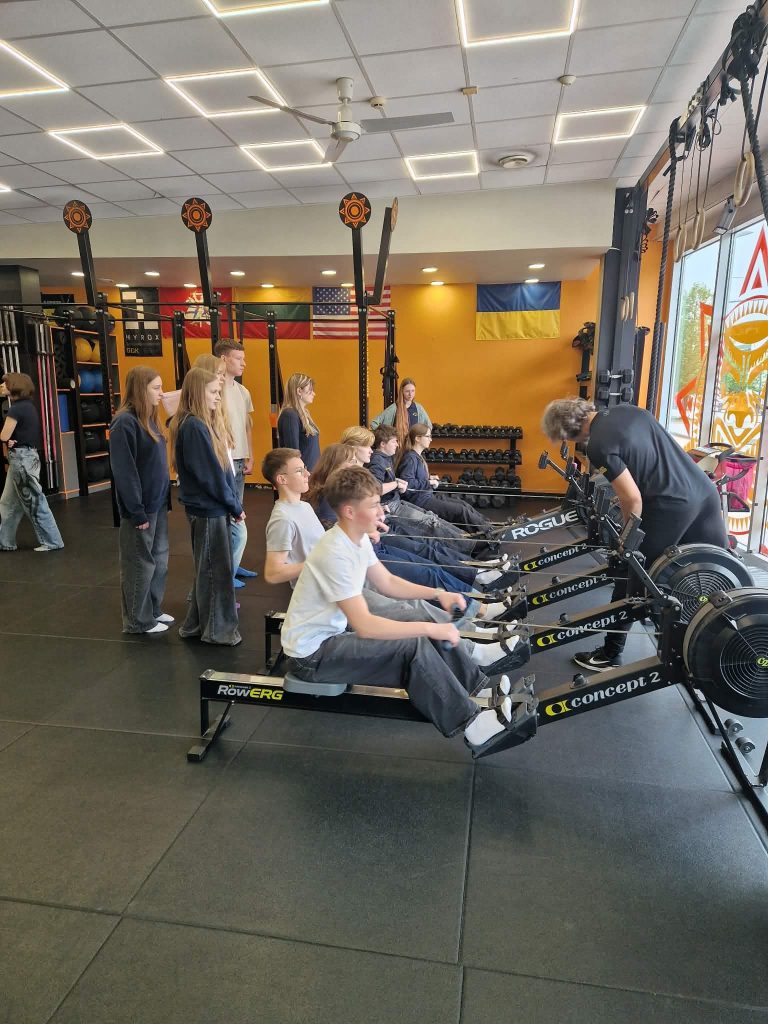 Students participating in a rowing exercise session at a fitness facility, focusing on healthy lifestyle activities as part of the "A Billion Steps Challenge" (BISTEPS) project.