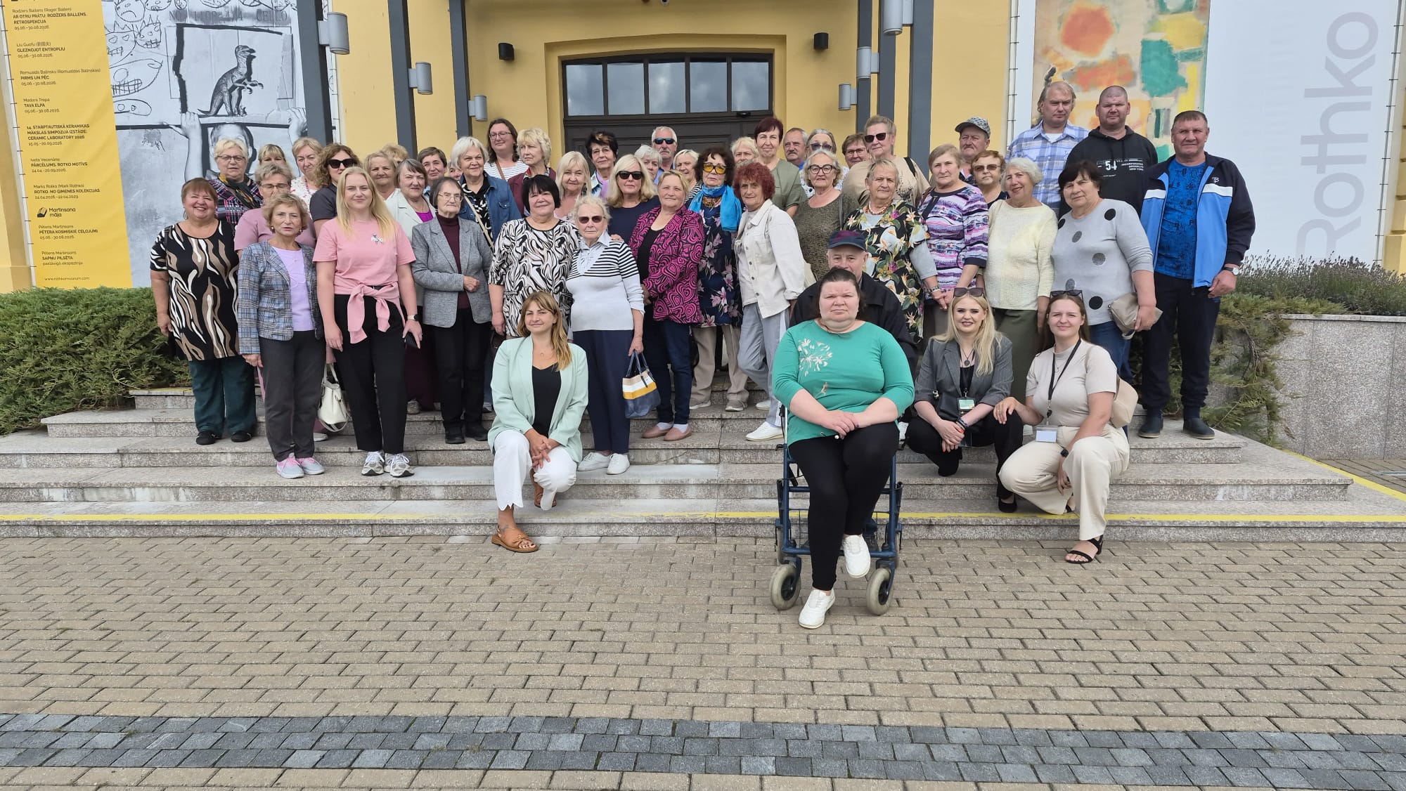 Group of Latvian and Lithuanian seniors gathered in front of a cultural center in Augšdaugava Municipality, showcasing their engagement in local traditions and health practices. Group of Latvian and Lithuanian seniors gathered in front of a cultural center in Augšdaugava Municipality, showcasing their engagement in local traditions and health practices.