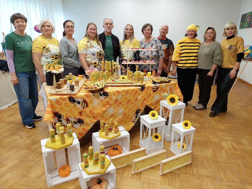 Group of participants at the SoCreative Project meeting in Latvia, dressed in bee-themed attire, standing in front of a colorful display of handmade crafts, candles, and floral arrangements, showcasing creativity and community spirit. Group of participants at the SoCreative Project meeting in Latvia, dressed in bee-themed attire, standing in front of a colorful display of handmade crafts, candles, and floral arrangements, showcasing creativity and community spirit.