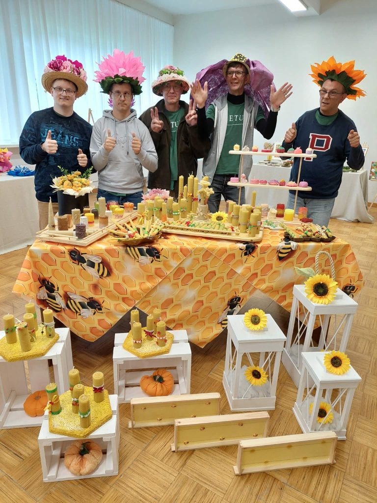 Participants at the SoCreative Project Meeting in Latvia showcase their creativity with colorful flower hats and handcrafted decorations, including candles and sweet treats, set against a vibrant honeycomb-themed tablecloth. Participants at the SoCreative Project Meeting in Latvia showcase their creativity with colorful flower hats and handcrafted decorations, including candles and sweet treats, set against a vibrant honeycomb-themed tablecloth.