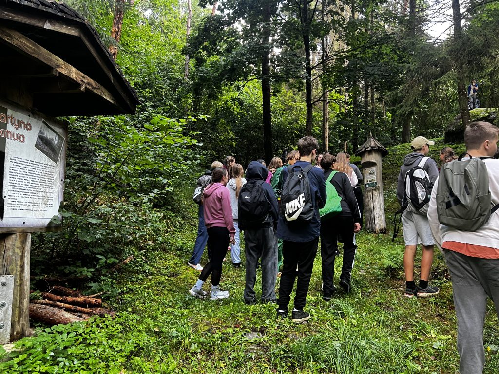 Students participating in outdoor activities related to the Healthy Lifestyle “A Billion Steps Challenge” (BISTEPS) project, walking along a forest path with informational signs in a lush green environment.