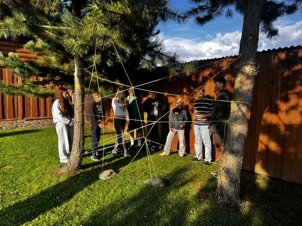 Group of participants engaged in a team-building activity, navigating a web of ropes between two trees, during the "A Billion Steps Challenge" (BISTEPS) project aimed at promoting healthy lifestyles.