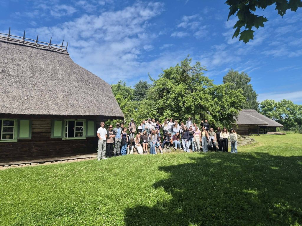 Group of people gathered in front of traditional thatched-roof houses, surrounded by green grass and trees, showcasing cultural heritage during an outdoor adventure experience. Group of people gathered in front of traditional thatched-roof houses, surrounded by green grass and trees, showcasing cultural heritage during an outdoor adventure experience.