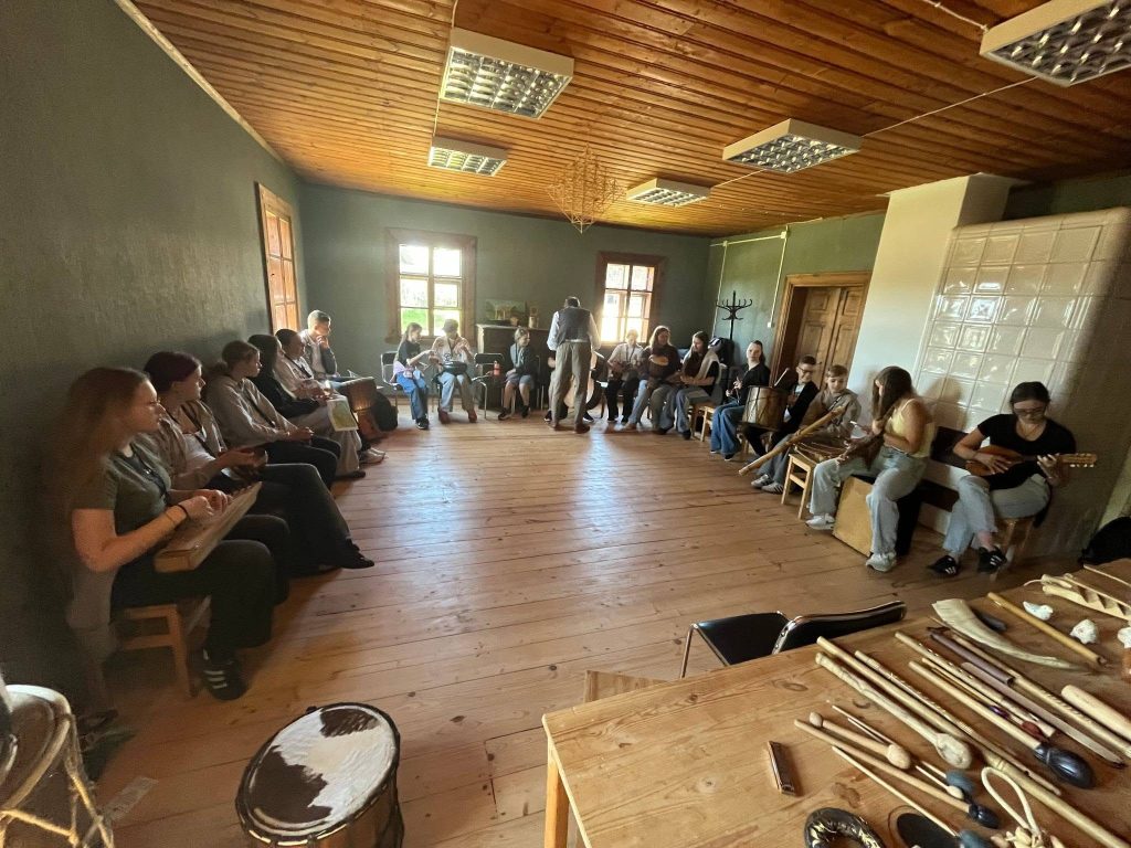 Group of participants engaged in a traditional music workshop, seated in a rustic room with wooden floors and a cozy atmosphere, surrounded by various musical instruments. Group of participants engaged in a traditional music workshop, seated in a rustic room with wooden floors and a cozy atmosphere, surrounded by various musical instruments.